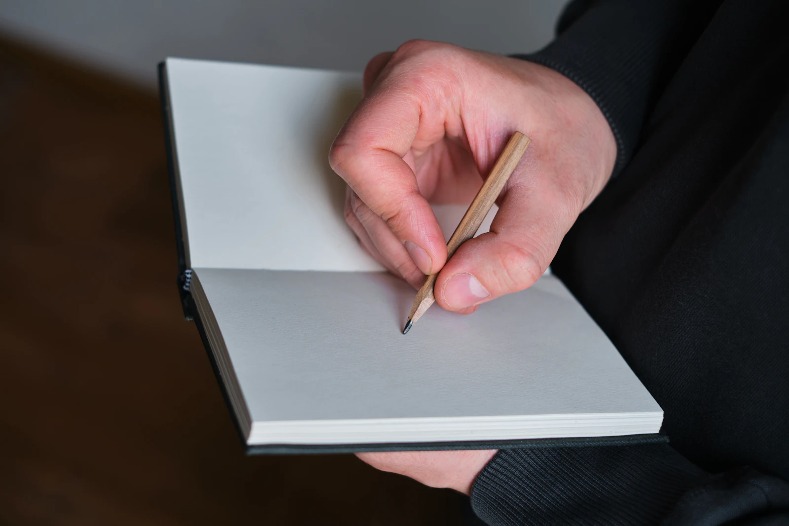 A hand writing in an open notebook with a pencil