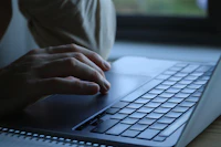 Person typing on a laptop keyboard by a window